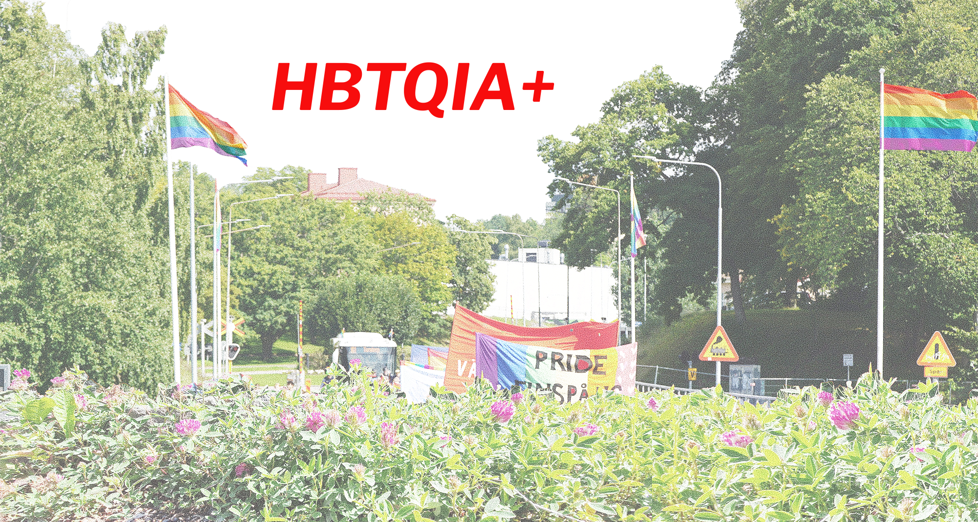 I bakgrunden grönska och några byggnader samt regnbågsflaggor och en Prideparad i mitten där endast delar av några banderoller är synliga. Rödklöver i förgrunden. Text i bild: HBTQIA+. 